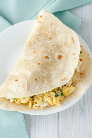 breakfast egg burrito with cheese,  herbs and spices on white plateの写真素材