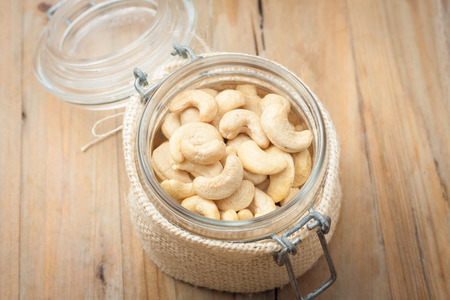 raw unsalted cashew nuts in glass jar on wooden rustic background, top viewの写真素材