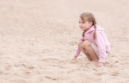 little girl with pig tails kneeling on the sand and looking aheadの写真素材