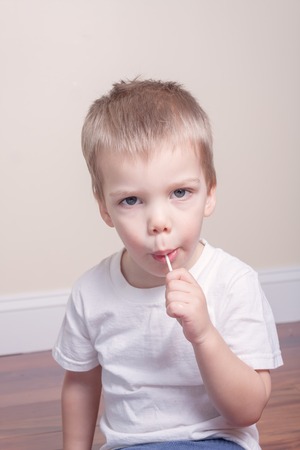 little boy with blond hair in white tshirt sucking lollipop in his mouthの写真素材