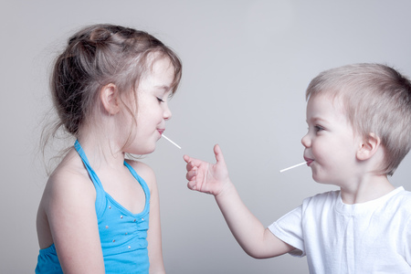 siblings having fun with lollypops - little brother is trying to grab his sister's lollypop, horizontal imageの写真素材