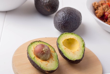 a ripe avocado cut in half with a pit still inside on wooden chopping board