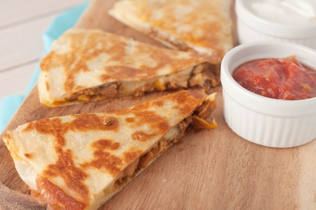 homemade chicken mexican quesadilla on wooden chopping board with a side of salsa served in white bowlの写真素材