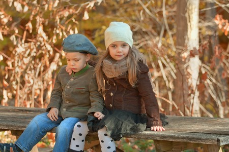Brother and sister dressed up warm in hats sitting on a bench in a park on a cool autumn dayの写真素材
