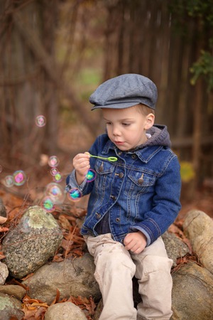 a little boy wearing a denim jacket and a hat blowing bubbles outdoors, vertical imageの写真素材