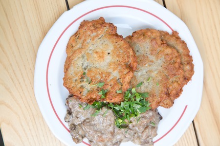 two large potato latkes served with mushroom thick sauce on white plateの写真素材