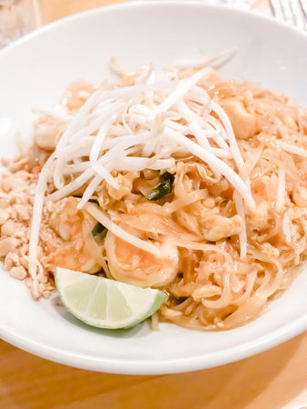 Traditional Thailand dish pad Thai served on a white shallow bowl topped with bean sprouts with lime...