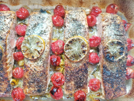 Grilled salmon fillets with lemon and cherry tomatoes on baking trayの写真素材