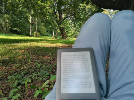 A woman reading a book in a public park, sitting under a treeの写真素材