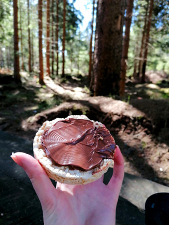 A woman holds a sandwich with chocolate spread in her hand in the forest.の写真素材