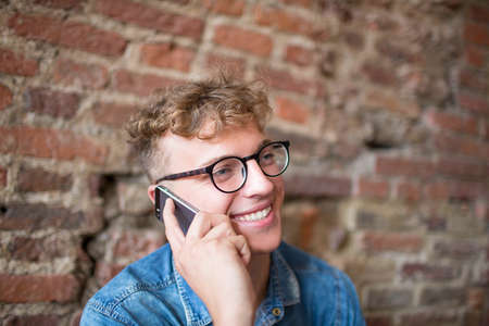 Young smiling hipster guy talking on portable mobile phone. Handsome happy man having pleasant cell...