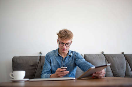 Young man modern businessman reading text message on mobile phone, holding touch pad in hand....