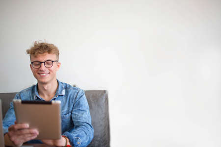 Smiling hipster guy having video call in internet via touch pad, sitting near copy space for your...