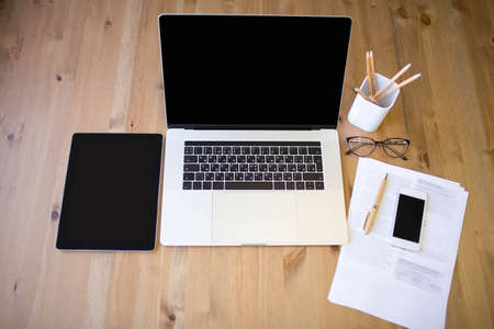 Modern workplace with contemporary laptop computer with touch bar, digital tablet and smart mobile phone. Desktop with portable open notebook, touch pad and cell telephone. Paper documents on tableの写真素材
