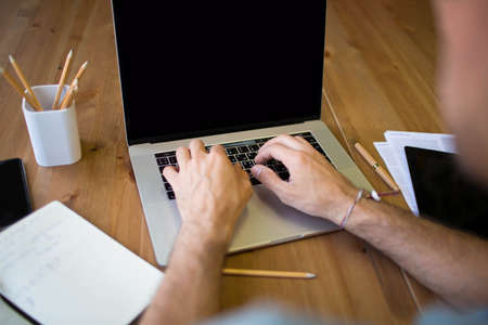 Man support specialist keyboarding on laptop computer, sitting at desktop with working tools. Male...