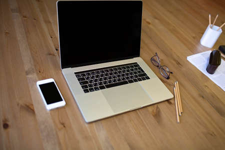 Wooden table with open laptop computer and mobile phone with copy space on screens. Workspace with...
