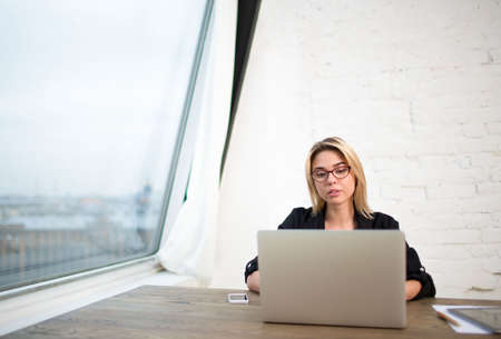 Young woman skilled IT support specialist working on laptop computer, sitting in office interior...