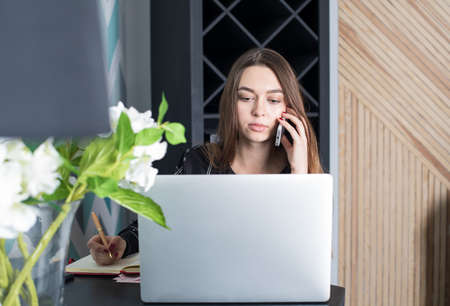 Confident woman owner coffee shop using laptop computer for search new employees, calling via mobile phone. Beautiful female student learning online via net-book, talking on smartphone. Hipster girlの写真素材
