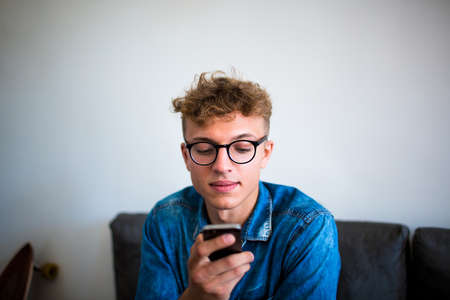 Stylish hipster guy using application on mobile phone, sitting in cafe. Fashionable man in glasses...