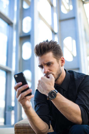 Excited trader worries following via cellphone about the prices on the stock exchange, sitting in company.Frustrated entrepreneur having problem, reading via mobile negative feedback about his projectの写真素材