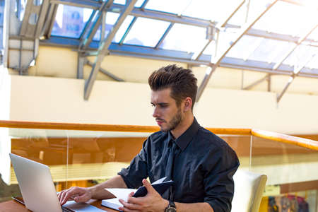 Serious man successful financier using textbook and laptop computer, sitting in company. Thoughtful...