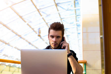 Confident man skilled boss talking via mobile phone and reading information on web site via laptop...