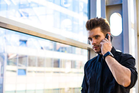 Pondering man financier in formal wear calling via smartphone while standing in business center near...