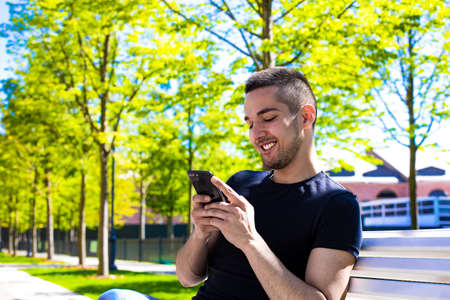 Smiling man university student watching funny video in internet via mobile phone while resting on a...