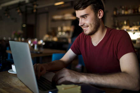 Young smiling man university student having online education via laptop computer while sitting in...