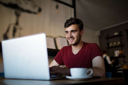 Happy smiling hipster guy having video conference via laptop computer while sitting in coffee shop....
