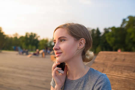 Young woman university student talking via mobile phone gadget while resting outdoors after education. Pretty women having pleasant cellphone conversation during rest in parkの写真素材