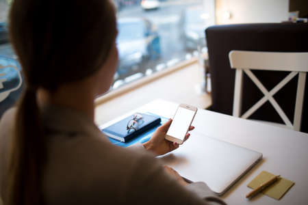 Female lawyer reading notification on mobile phone with empty copy space screen background for promotional text message while sitting at workplace with laptop computer and textbookの写真素材