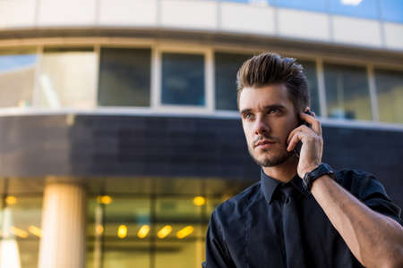 Handsome man skilled lawyer talking with client via mobile phone while standing outdoors against business center background with copy space for promotional content.Men banker phoning via cellphone pdaの写真素材
