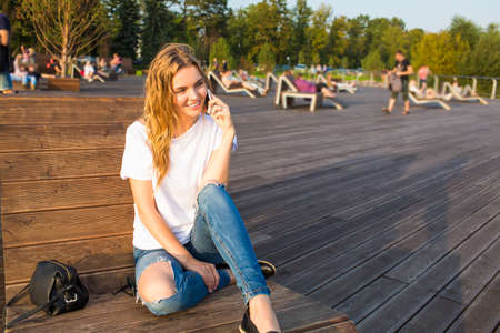 Happy smiling hipster girl having funny mobile phone conversation with friend while sitting in park...