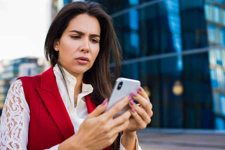 Frustrated business woman received bad news in e-mail on mobile phone while standing outside company...