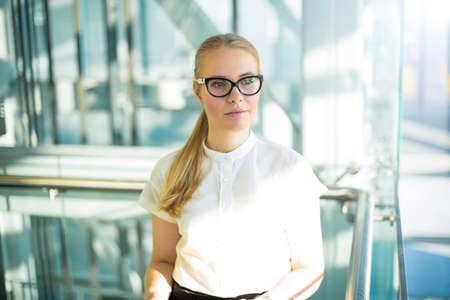 Thoughtful business woman in formal wear and glasses thinking about new work ideas while standing in modern office corporation interior. Pensive female lawyers dreaming during break at jobの写真素材