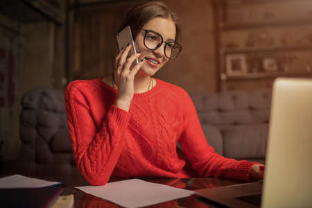 Smiling woman skilled creative writer dressed in cool outfit wear talking via cell telephone and...