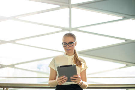 Proud woman entrepreneur in glasses and formal wear reading e-mail on portable touch pad device...