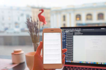 Closely woman content writer holding mobile phone with blurred text message on the screen during online learning via pc laptop computer while relaxing in coffee shop during recreation time in holidaysの写真素材