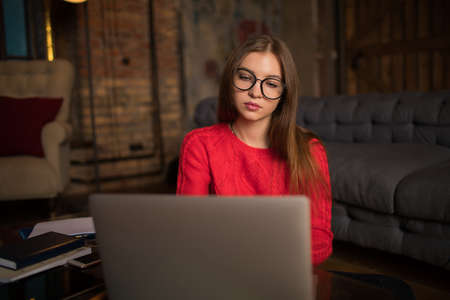 Serious woman freelance business planning expert working on laptop computer, sitting inside home interior. Female in spectacles skilled trader using netbook for job. Online education via notebookの写真素材