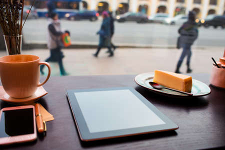 Modern touch pad lying on a wooden table in coffee shop near mobile phone and cup of latte. Digital tablet computer lying on a restaurant tableの写真素材