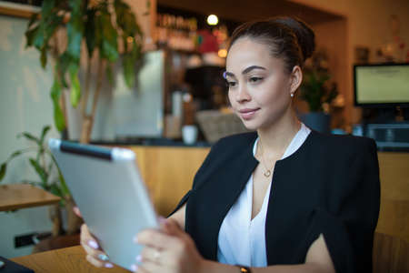 Young Caucasian female smart university student online learning via portable touch pad while sitting...