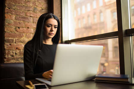 Serious confident business woman having online training course on laptop computer, sitting in restaurant during break in company. Female proud financier using applications on notebook, resting in cafeの写真素材