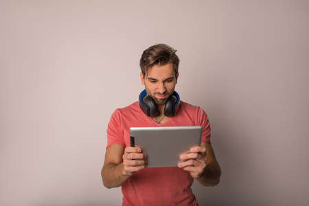 Young man having an exciting online game via portable touch pad computer while standing isolated in...