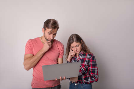 Two pensive colleagues man and woman with pensive look reading interesting information on portable...