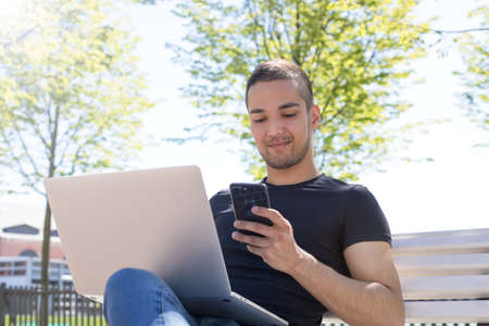 Young stylish hipster guy smart university student reading article in social network via cellphone...