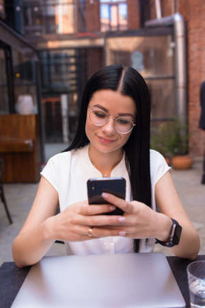 Charming business woman online ordering via mobile phone while sitting in coffee shop during...