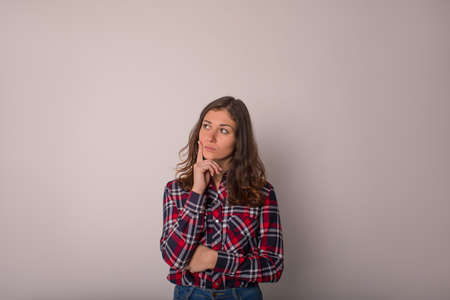 Young female student with pensive look holding finder on the face and thinking about something while standing isolated in studio against wall background for promotional contentの写真素材