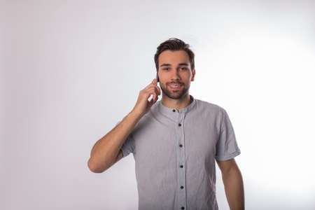 Portrait of a happy smiling bearded business man talking via mobile phone while standing isolated in studio against wall background with copy space for promotional contentの写真素材