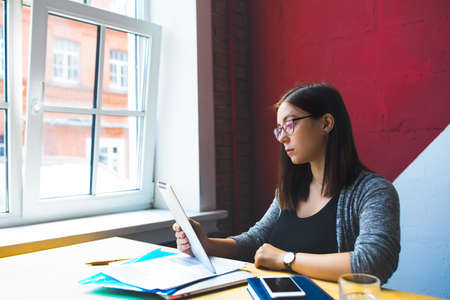 Female successful business worker checking e-mail on touch pad while sitting in office interior near...